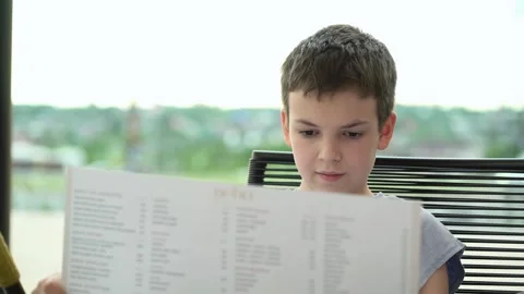A young boy reading a menu while sitting on a bench at a restaurant's  Stock-Footage 336822819