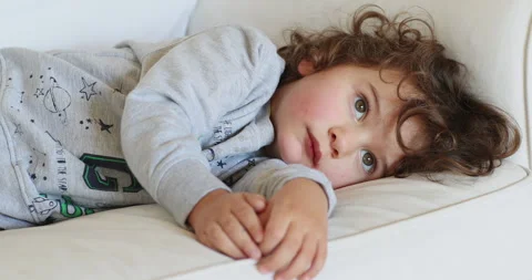 Young boy resting on a white sofa, looking unwell and tired Stock-Footage 272590174