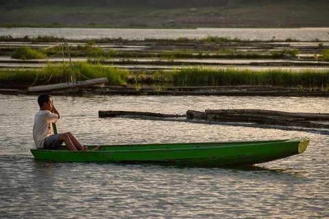 A young boy rides a small rowing boat on a calm lake. Stock Photos