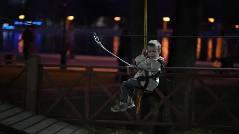 Young boy riding a zip line in an outdoor rope park, enjoying an exciting Stock Footage 345936741