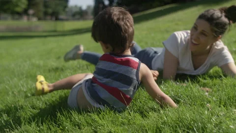 A young boy rolls down a grassy hill with his mom while playing at the park 動画素材 143629587