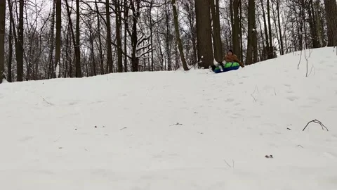 The young boy rolls on a tube in a winter park, the tube flies over the camera Stock Footage