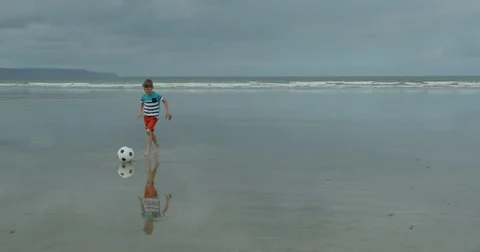A young boy runing along a beach playing soccer. Vídeo Stock 79794483