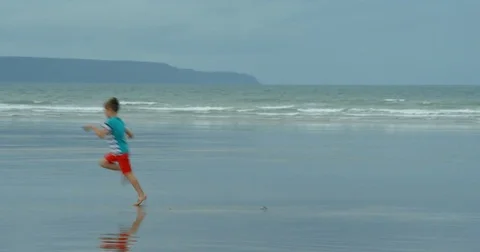 A young Boy Running on a beach looks back at his footprints. 스톡 동영상 79792834