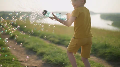 Young Boy Running with Bubble Gun in a Sunny Field by a Lake 스톡 동영상 285561953