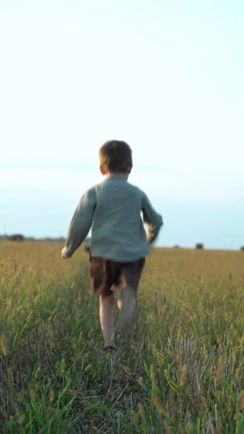 Young boy runs freely through golden grassy field with hay bales 스톡 동영상 343138434