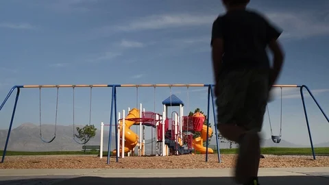 Young boy runs to the swing set at a playground by himself. Stock Footage 94930257