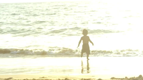 A young boy runs towards the ocean and jumps into the waves Stock Footage 33894451