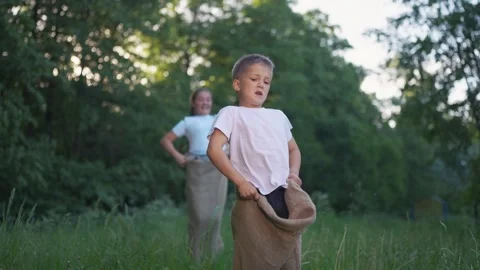 Young boy in sack. Boy is racing a sack of grass outdoors. A young girl jumps in Stock Footage 318009502
