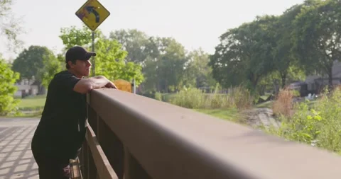 A young boy with a sad expression is leaning on a bridge in the park, looking up Stock-Footage 347026511