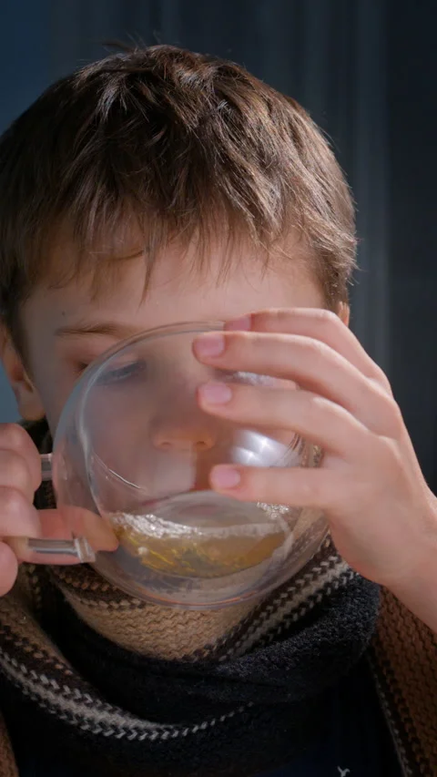 Young boy in scarf drinking hot tea from glass cup Stock Footage 325629330