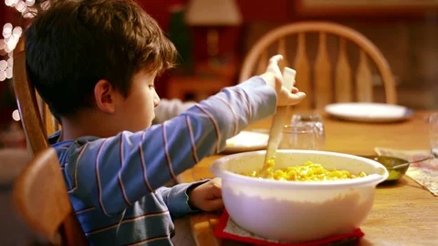 Young boy scooping macaroni and cheese onto plate at dinner table Stock Footage 71048629