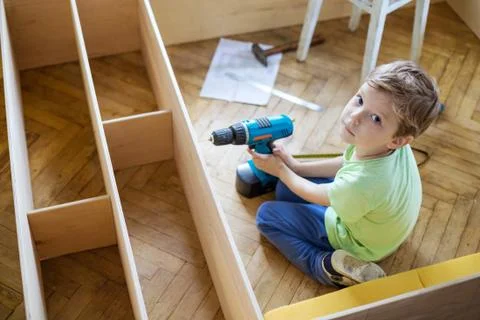 Young boy with screwdriver looking up while sitting on floor Stock Photos