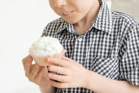 A young boy in a shirt eats a cake on a light background. The food joy of swe Stock Photos