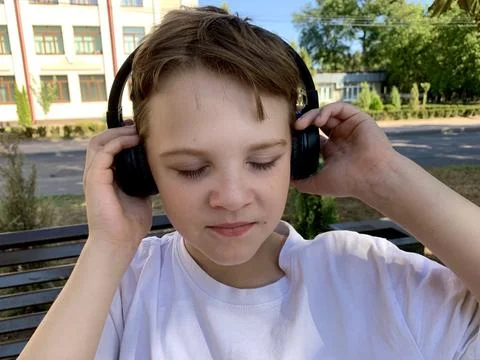 A young boy sits on a bench in a peaceful neighborhood, completely immersed in Stock Photos