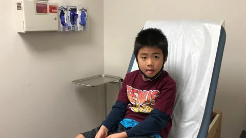 Young boy sits on exam table alone, waits to be examined by doctor. Stock Footage 131401369