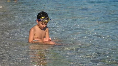 Young boy sits in shallow sea waters Stock Footage 202628997