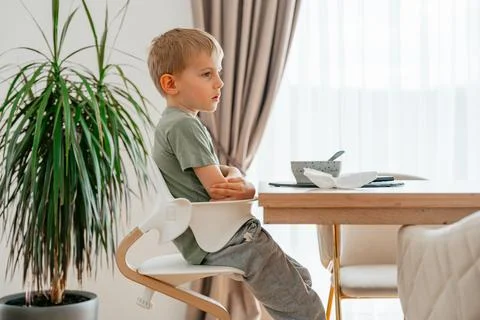 Young boy sits at a table with an expression of distraction while a bowl of Foto stock