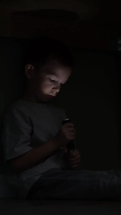 Young boy sits under the table in total darkness shining a flashlight directly Stock Footage 346305700