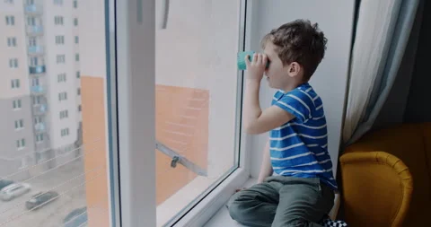 A young boy sits by a window, exploring the world with binoculars Stock Footage 307296518