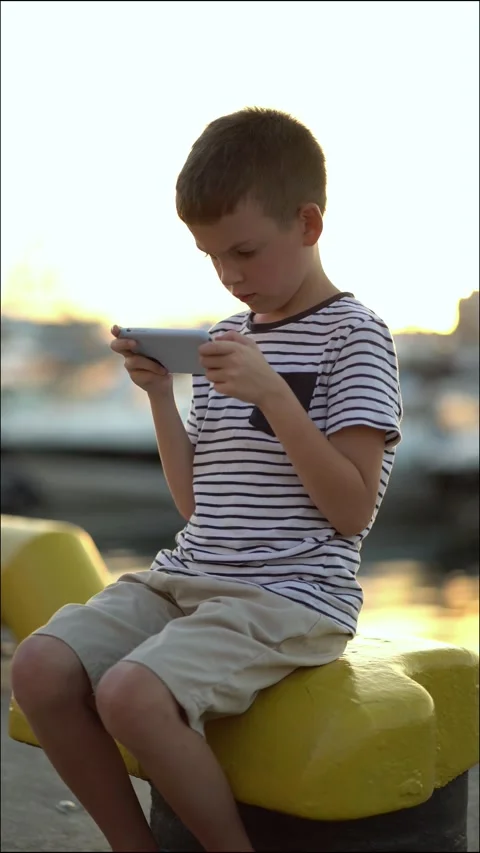 A young boy sits on a yellow structure at the harbor during golden hour Stock-Footage 337006321