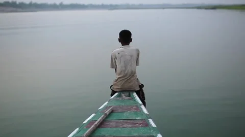 Young boy sitting alone on a boat sailing a calm river Stock-Footage 333204536