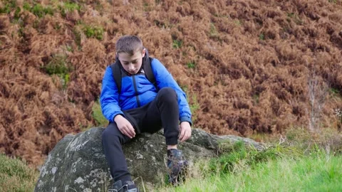 Young boy sitting and resting, fastening his walking boots, in a autumn out.. Stockbeeldmateriaal 254803333