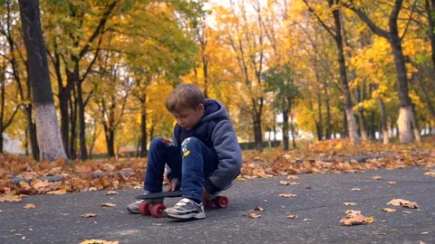 Young boy sitting and rolling on skateboard Stock Footage 98658961
