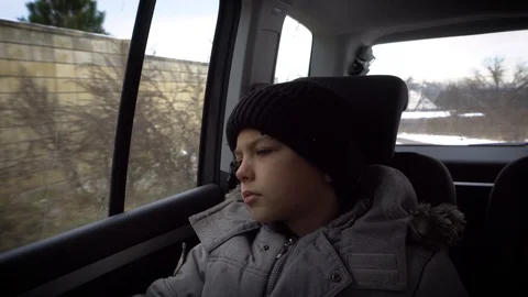 Young Boy Sitting on the back seat in a car listening to music and looking Stock Footage 98694071