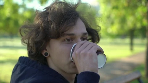 Young boy sitting on a banch and drink coffee in the morning in the park, 4k 库存影片 95498397