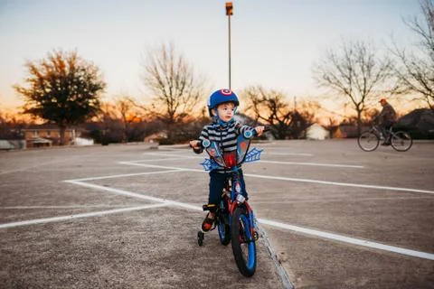 Young boy sitting on bike in parking lot with grandfather riding Stock Photos