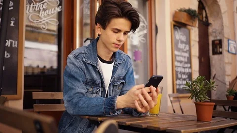 Young boy sitting in cafe use phone drink juice smile feel happy outdoor guy Stock Footage 92052500