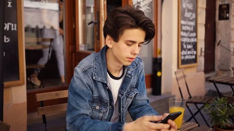 Young boy sitting in cafe use phone look at camera smile feel happy outdoor guy Stock Footage 92052568