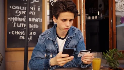 Young boy sitting in cafe use phone and credit card drink juice portrait outdoor Stock Footage 92052768