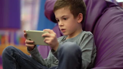 Young boy sitting comfy soft violet armchair and play telephone gaming Stock-Footage 230215461