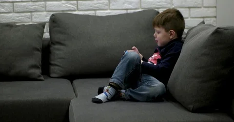 Young Boy Sitting on the Couch and Playing Games on the Smart Phone. 動画素材 71793132