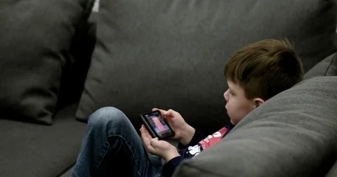 Young Boy Sitting on the Couch and Playing Games on the Smart Phone. 動画素材 71793139