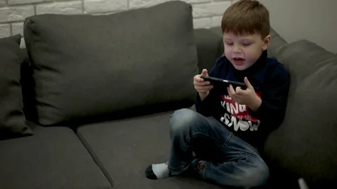 Young Boy Sitting on the Couch and Playing Games on the Smart Phone. Stock Footage 71793238