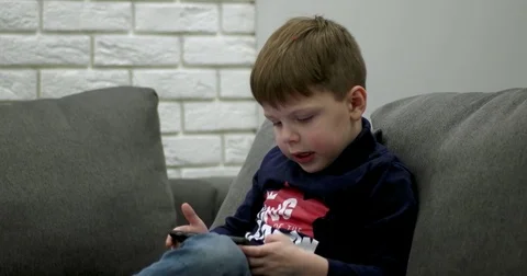 Young Boy Sitting on the Couch and Playing Games on the Smart Phone. Video stock 71793361