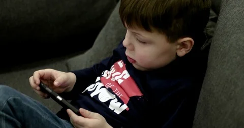 Young Boy Sitting on the Couch and Playing Games on the Smart Phone. 動画素材 71800512