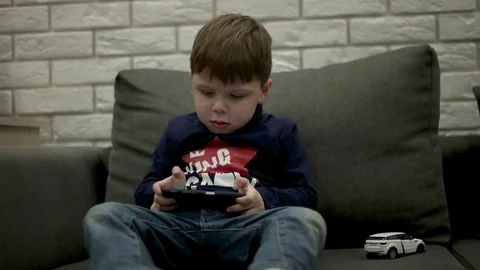 Young Boy Sitting on the Couch and Playing Games on the Smart Phone. Stockbeeldmateriaal 71982509