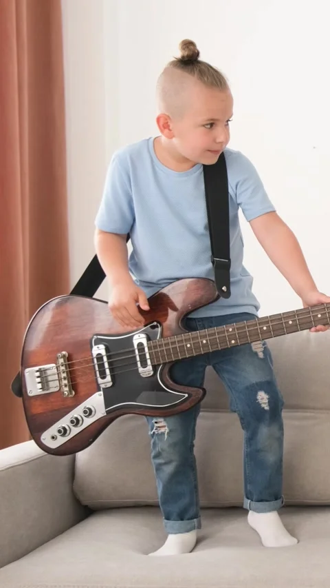 A young boy is sitting on a couch holding a guitar Stock Footage 264690660