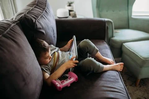 Young boy sitting on couch playing educational game on tablet Stock Photos