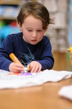 Young boy sitting down at desk indoors coloring with markers Stock Photos