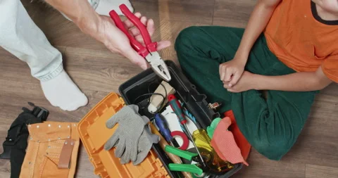 Young boy sitting on floor hands pliers from toolbox to father Vidéo 323968875