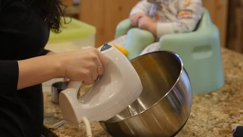 Young boy sitting on kitchen counter puts hands on ears as mixer is used Stockbeeldmateriaal 86814243