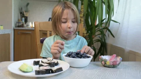 Young boy sitting at the kitchen table holding a blueberry with a bowl of Stock Footage 318221307