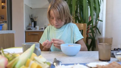 Young boy sitting at the kitchen table peeling and eating peanuts and pistachios Stock Footage 318222832