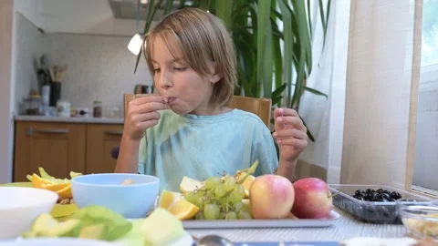 Young boy sitting at the kitchen table eating black olives with a tray of fresh Stock Footage 318228666