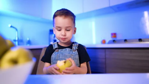 Young boy sitting in modern kitchen with blue lighting. A child wearing denim Stock Footage 342573988